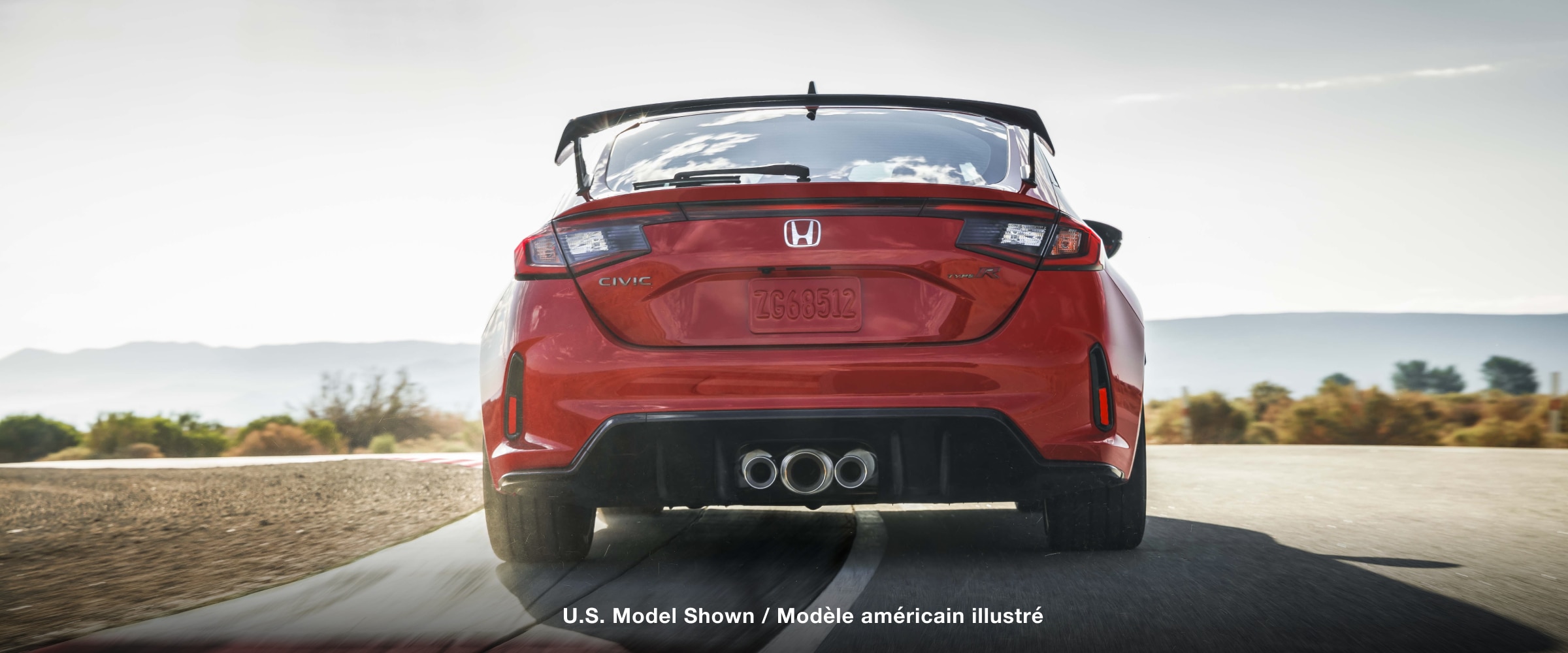 Straight on closeup of the triple centre exhaust on a red Type R racing on a track.