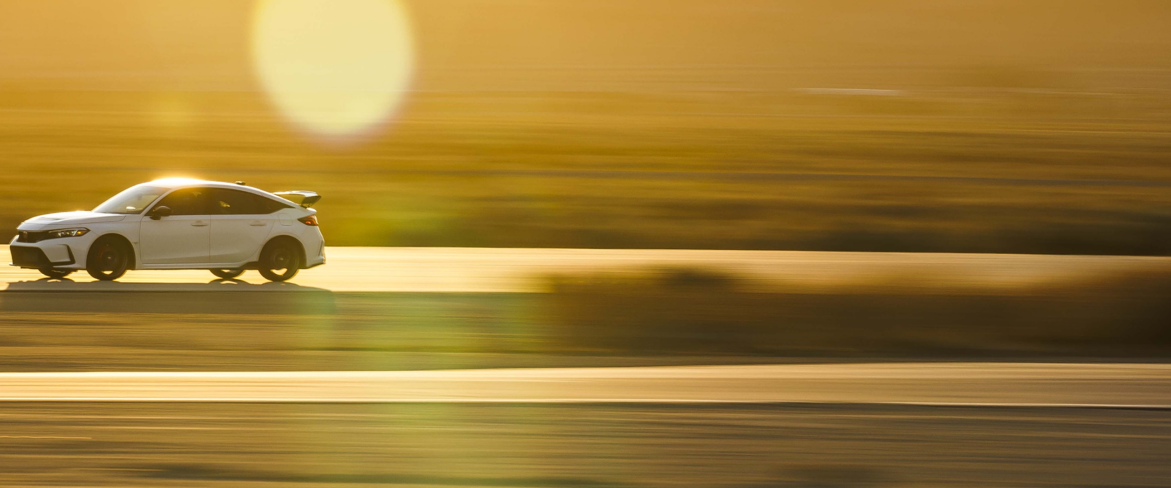 Wide shot and sideview of a white Type R driving down a highway during a desert sunset. Front is more visible.