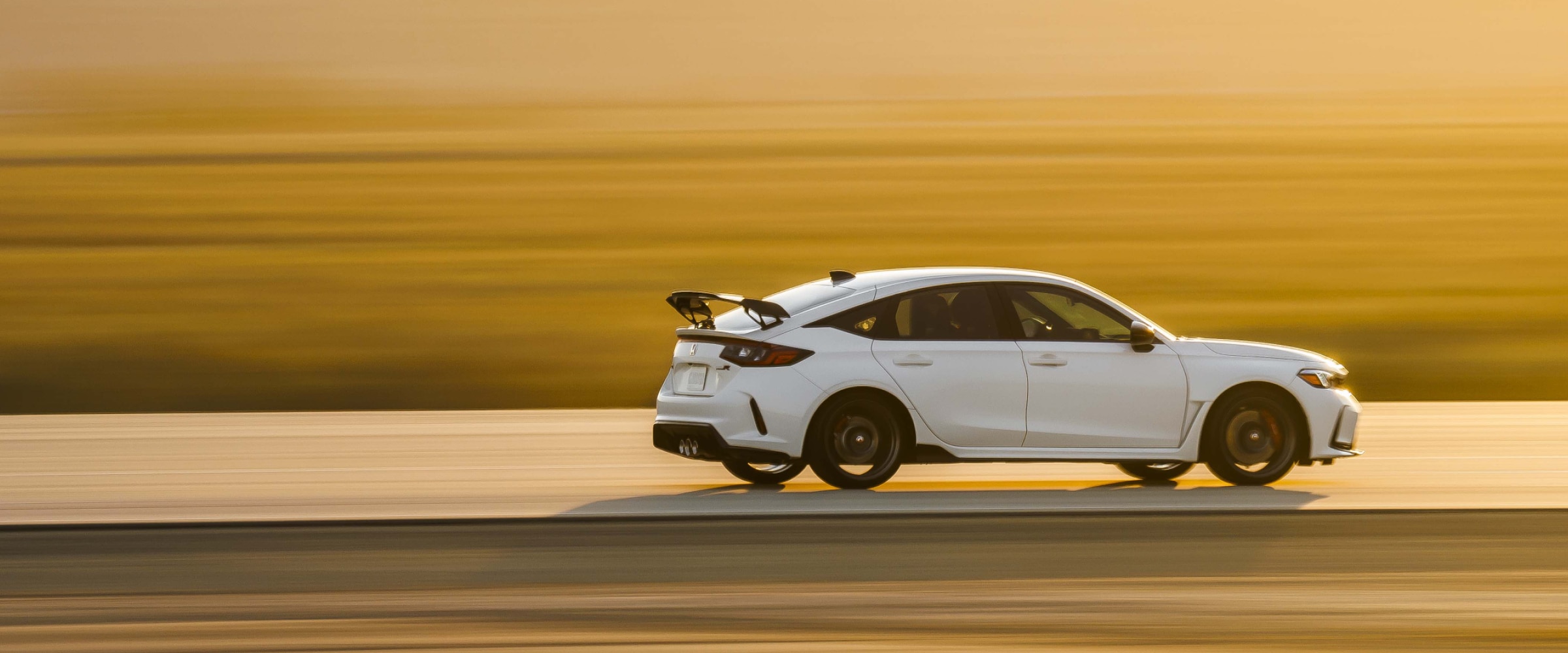 Wide shot and sideview of a white Type R driving down a highway during a desert sunset. Rear is more visible.