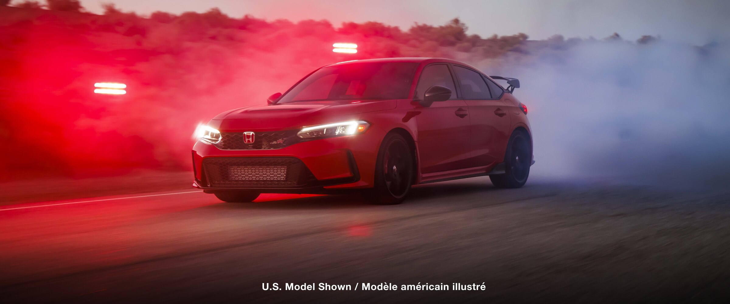 Plan de trois quarts de l’avant d’une Type R rouge qui démarre en trombe sur une route de désert à la nuit tombante.