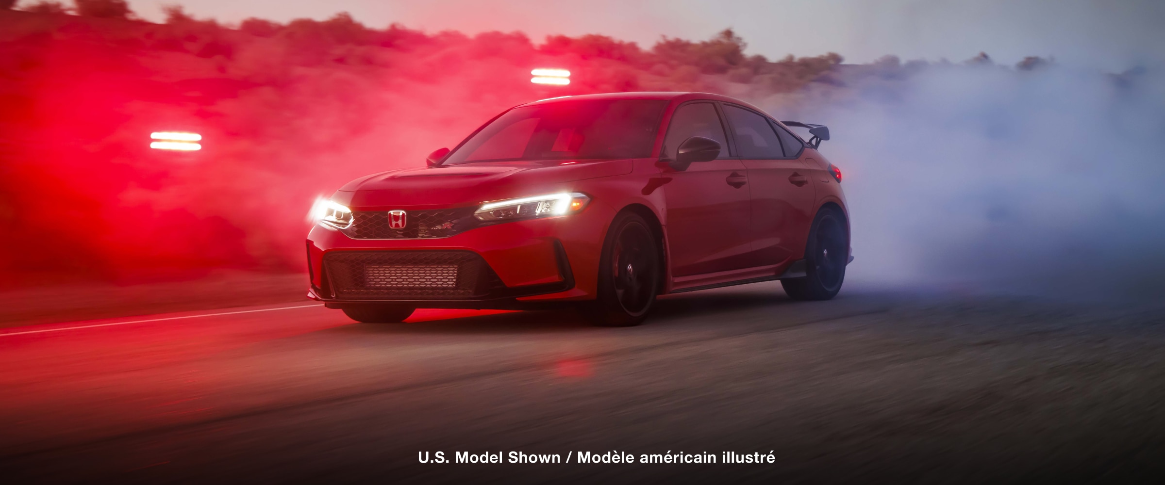 Plan de trois quarts de l’avant d’une Type R rouge qui démarre en trombe sur une route de désert à la nuit tombante.