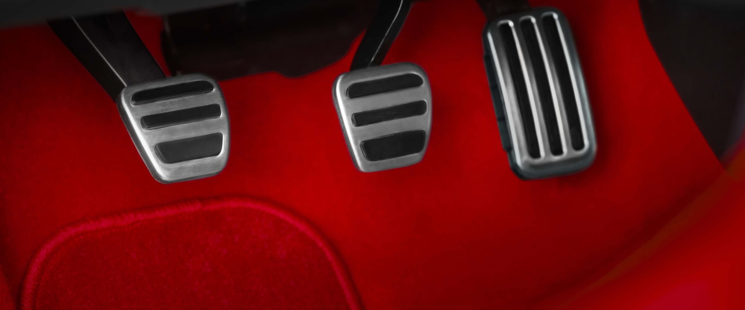 Closeup of aluminum-trimmed sport pedals and red felt footwell.