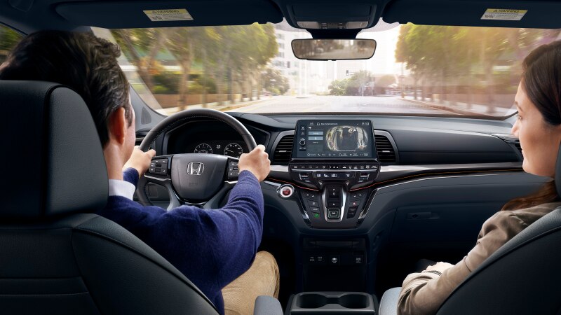 View from the backseat of a car with two adults up front and a rear-seat camera displayed on the dashboard screen.