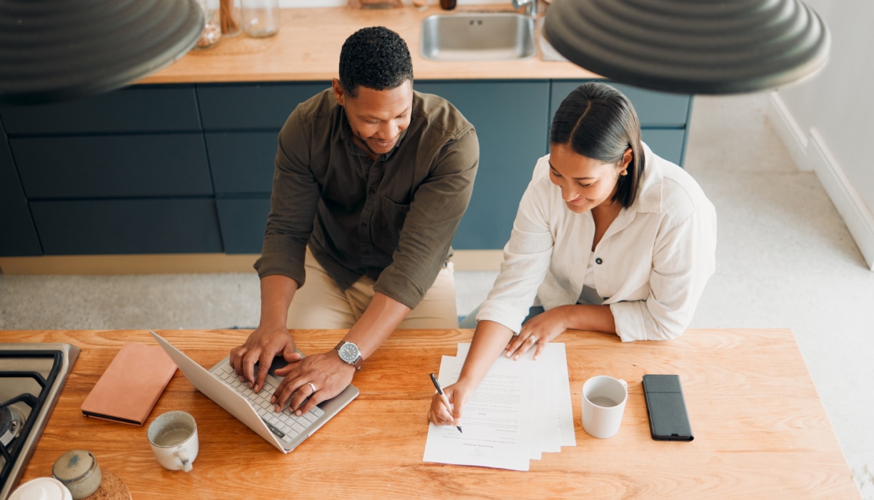 Deux adultes sont assis sur un canapé et consultent des documents en souriant.