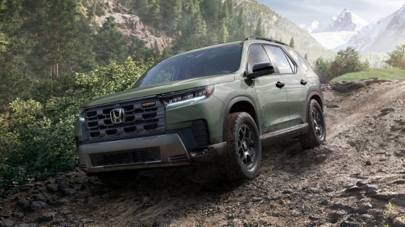 Plan de trois quarts avant d’un Pilot roulant sur un chemin de terre humide en déclin dans une forêt pluviale tempérée.  