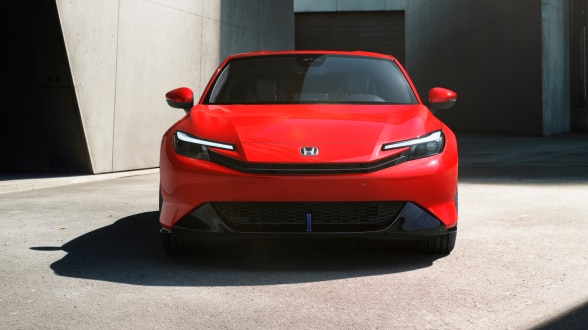 Vue avant d’une Prelude rouge garée au soleil entre des bâtiments aux murs de pierre.