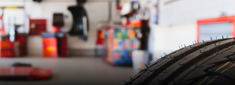 Closeup of a tire’s tread. In the background, out of focus, we see we’re in a mechanic’s shop.