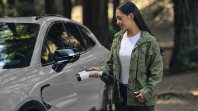 View of a woman plugging in a charging cord into a white Prologue in temperate forest.