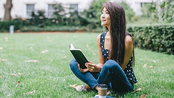 A young woman reading a book in a park./  Une jeune femme lisant un livre dans un parc