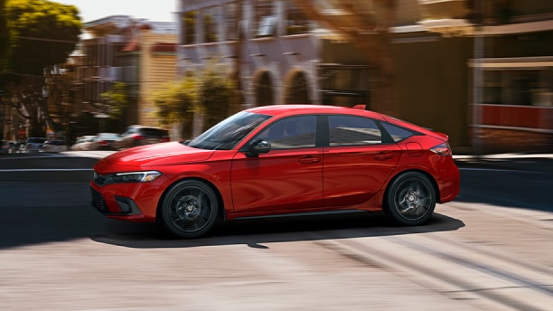 Sideview of red Hatchback driving on sunny city street.