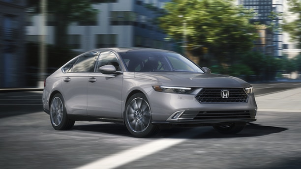 3/4 front view of grey Accord making a turn on a city street.