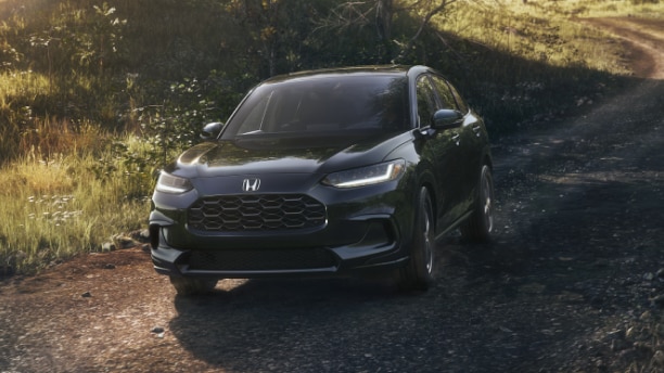 Plan de trois quarts avant d’un HR-V noir roulant vers la caméra sur une route de terre en campagne.