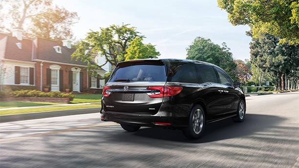 Rear view of a dark Honda Odyssey driving down a quiet residential street.