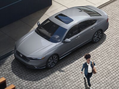 Plan de trois quarts en plongée d’une femme s’éloignant d’une Accord grise stationnée en bordure de rue dans un chic quartier urbain.