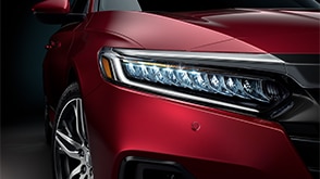 Close-cropped shot of the passenger-side headlight on a red Honda. // Plan rapproché du phare côté passager d'une Honda rouge.