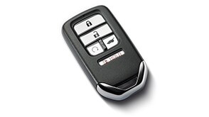 A Honda black remote entry key fob sitting on a white surface.	// Une télécommande porte-clés Honda noire sur une surface blanche.