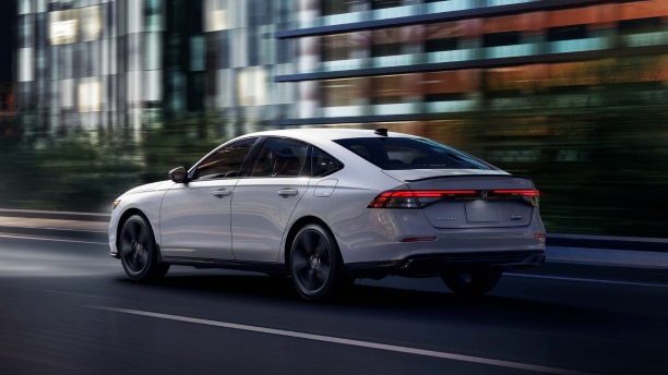 Plan de trois quarts arrière d’une Accord blanche circulant de nuit sur une autoroute devant des bâtiments.