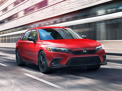 Rear left image of an Acura RDX that emphasises the spoiler and aesthetics of the vehicle while driving fast on the road causing the buildings in the background to blur. // Image arrière gauche d'un Acura RDX qui met l'accent sur le becquet et l'esthétique du véhicule tout en conduisant rapidement sur la route, ce qui rend les bâtiments à l'arrière-plan flous