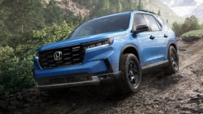 Plan de trois quarts avant d’un Pilot bleu pâle roulant sur un chemin de terre humide en déclin dans une forêt pluviale tempérée.  