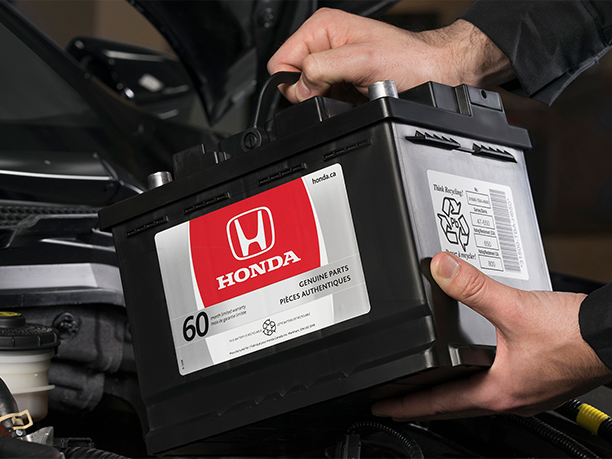 Close-up shot of Honda technician inserting a genuine Honda battery into an open car hood.  	Gros plan d’un technicien Honda insérant une véritable batterie Honda dans un capot de voiture ouvert. 
