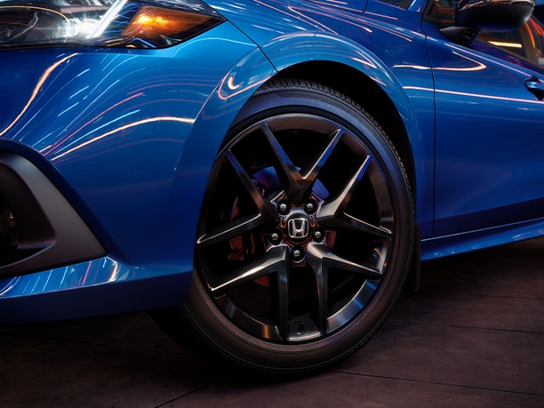 Low, angled shot of the front driver’s side of a blue Honda at night in the city with red and white lights reflecting off the glossy paint finish.	Plan bas et incliné du côté conducteur d’avant d’une Honda bleue pendant la nuit dans la ville avec des lumières rouges et blanches se reflétant sur la finition de peinture brillante.