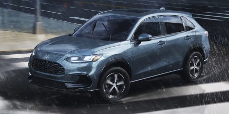 Plan de trois quarts latéral d’un HR-V forêt nordique nacrée roulant sous la pluie en ville.