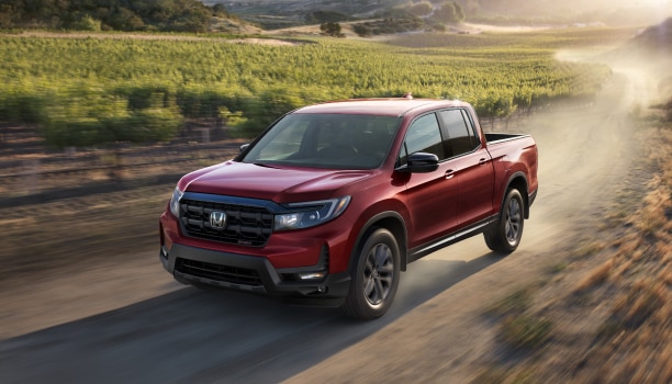 3/4 front view of red Ridgeline driving on dirt road in wine country.