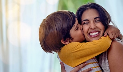 Une jeune mère qui reçoit un câlin et un bisou sur la joue d’un petit enfant.