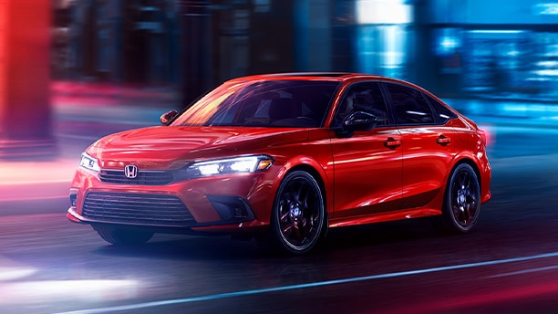 Front, driver-side angled view of a red Honda Civic driving through the city at night.