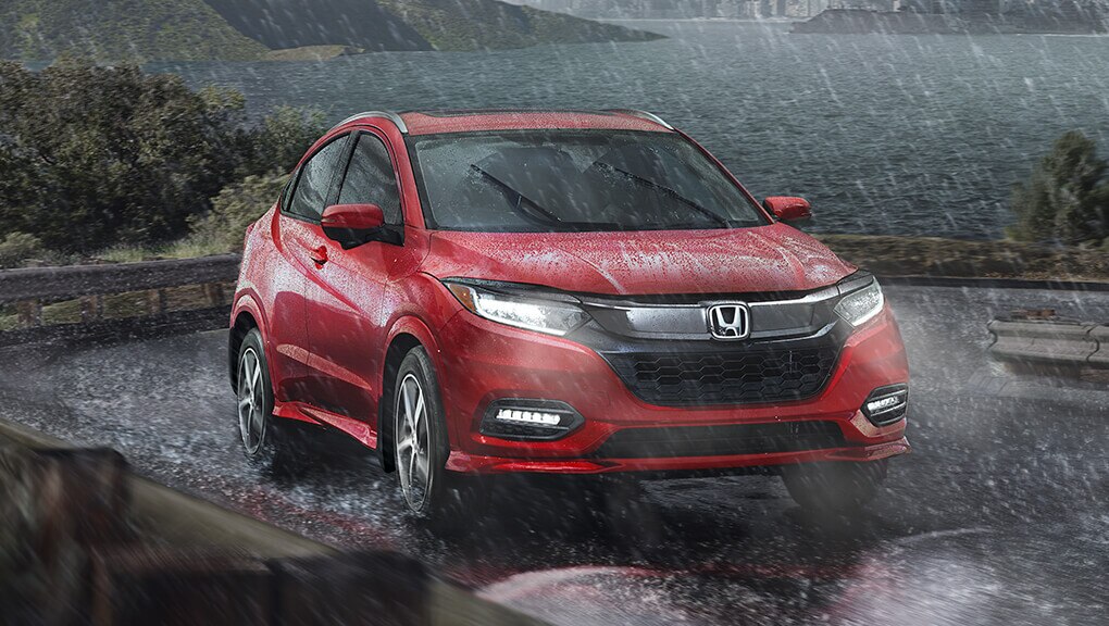 Front passenger-side view of the 2022 Honda HR-V in red driving on lakeside road in the rain. 