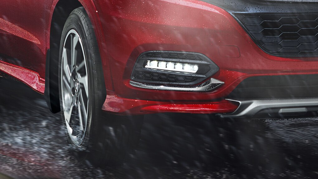 Gros plan des antibrouillards du Honda HR-V 2022 en rouge, conduite sous la pluie. 