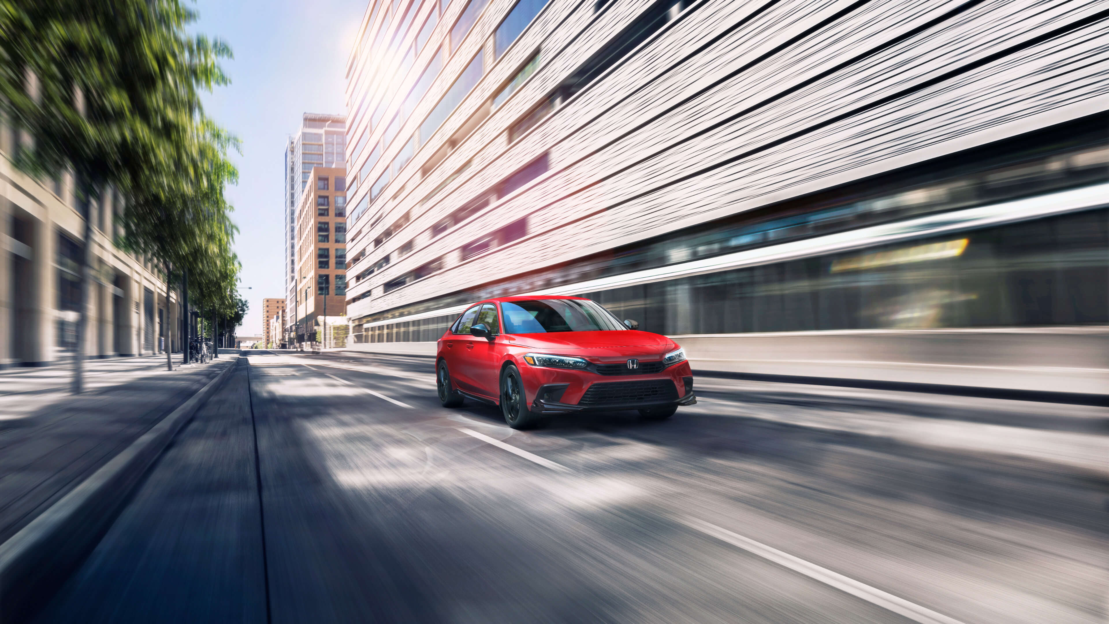 Slightly blurred by motion, front passenger-side, angled view of a red 2022 Honda Civic driving past a city block in the daytime.