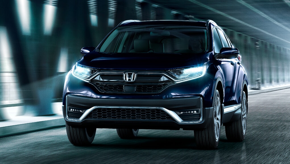 Front view of the 2021 Honda CR-V Touring in Obsidian Blue Pearl, driving under an urban overpass.