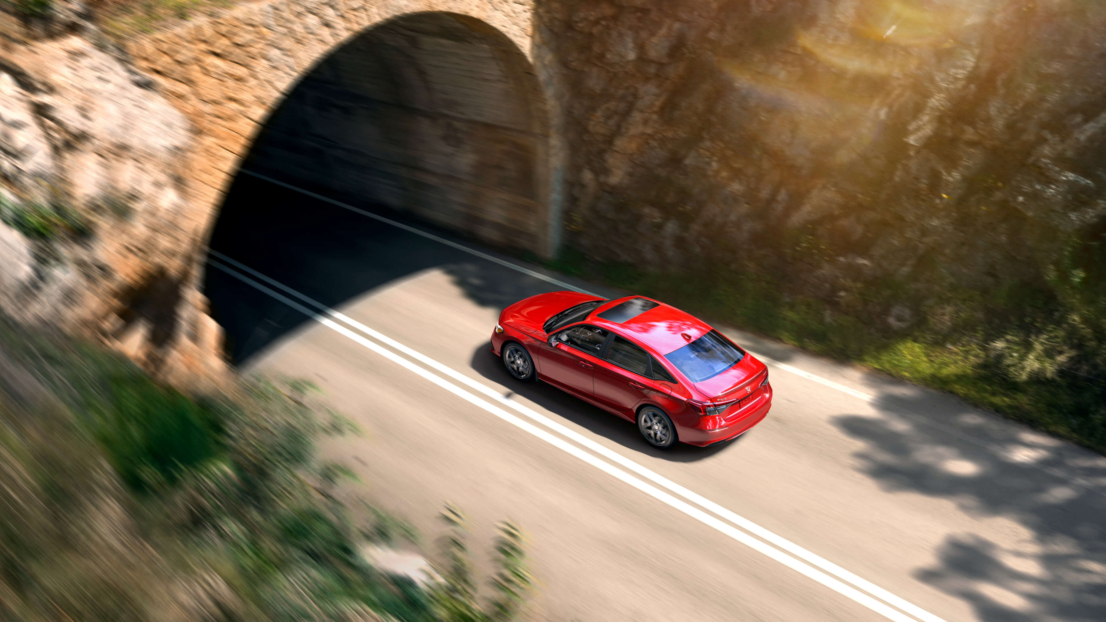 Plan panoramique en vue plongeante d’une Honda Civic 2022 rouge sur le point de traverser un tunnel en pierre.