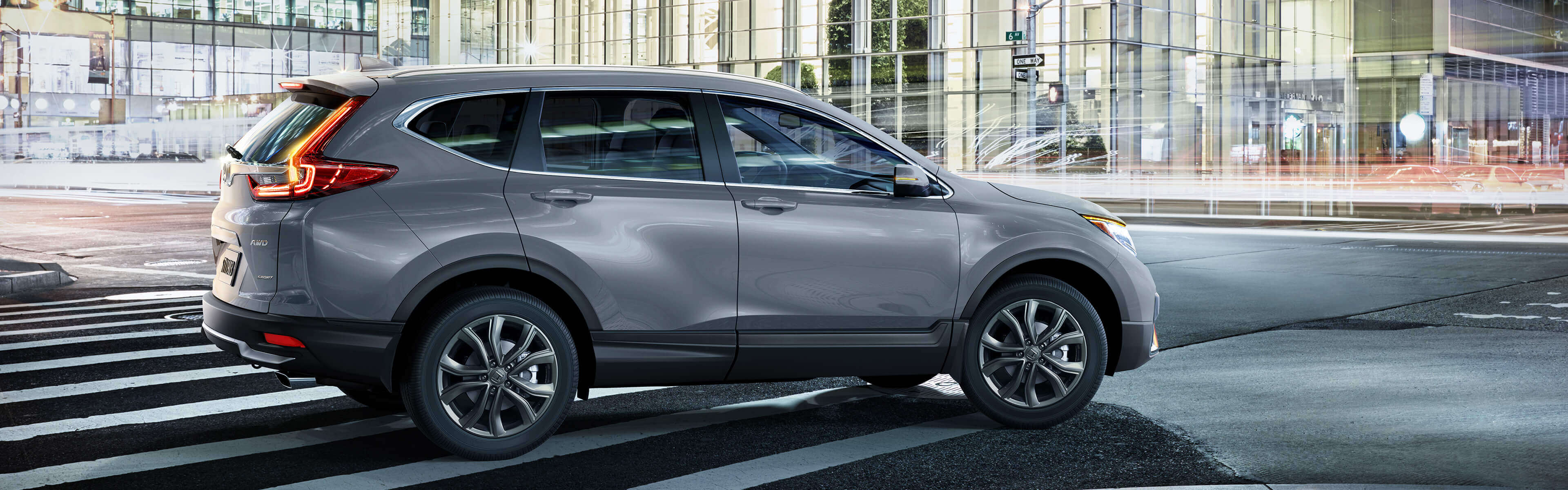 Passenger-side profile view of the 2021 Honda CR-V in Sonic Grey Pearl, driving in an urban environment at night.