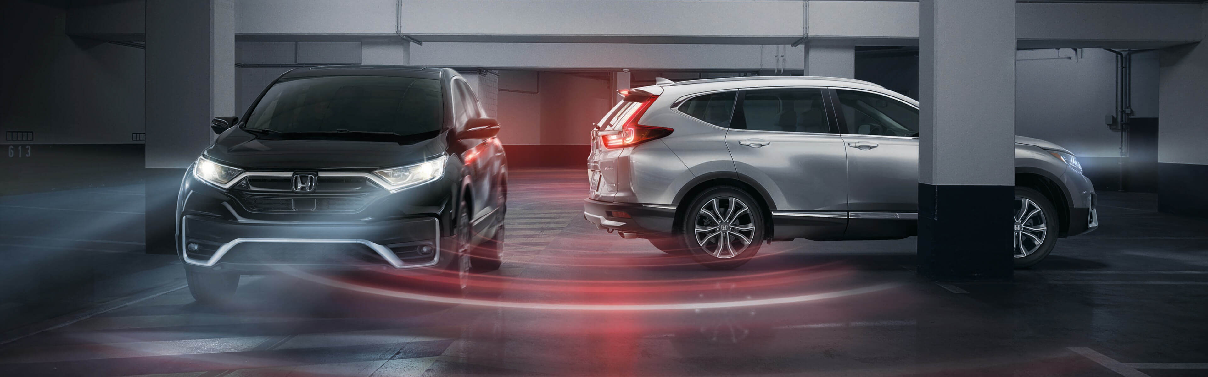 Passenger-side profile view of 2021 Honda CR-V Touring in Lunar Silver Metallic demonstrating cross traffic monitor in parking structure.