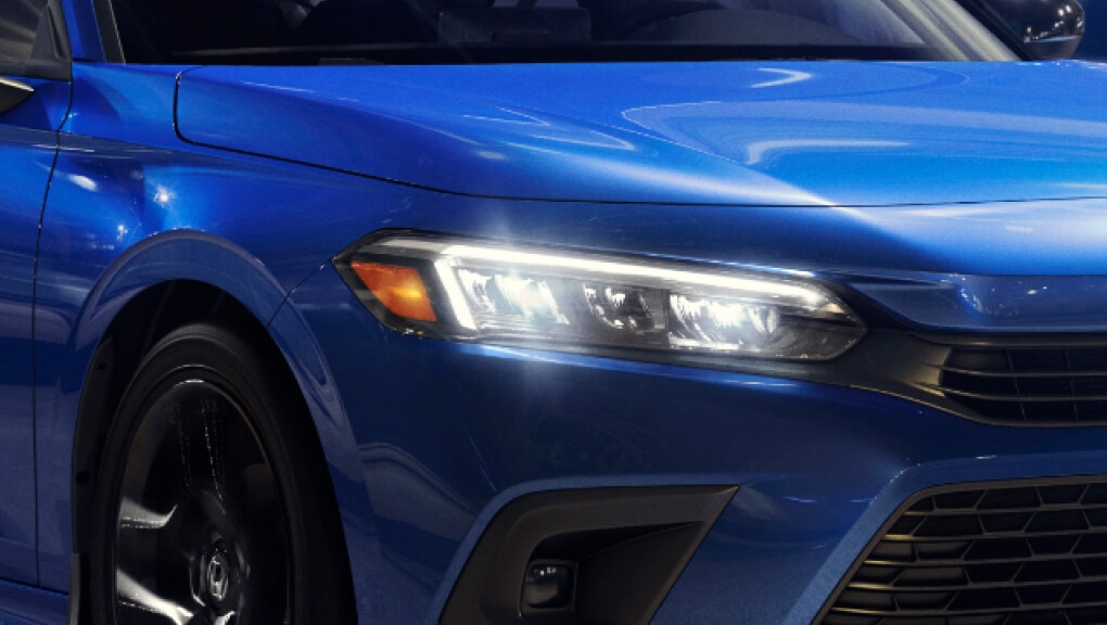 Side-angled close-up of a headlight on a blue 2022 Honda Civic shining at night.