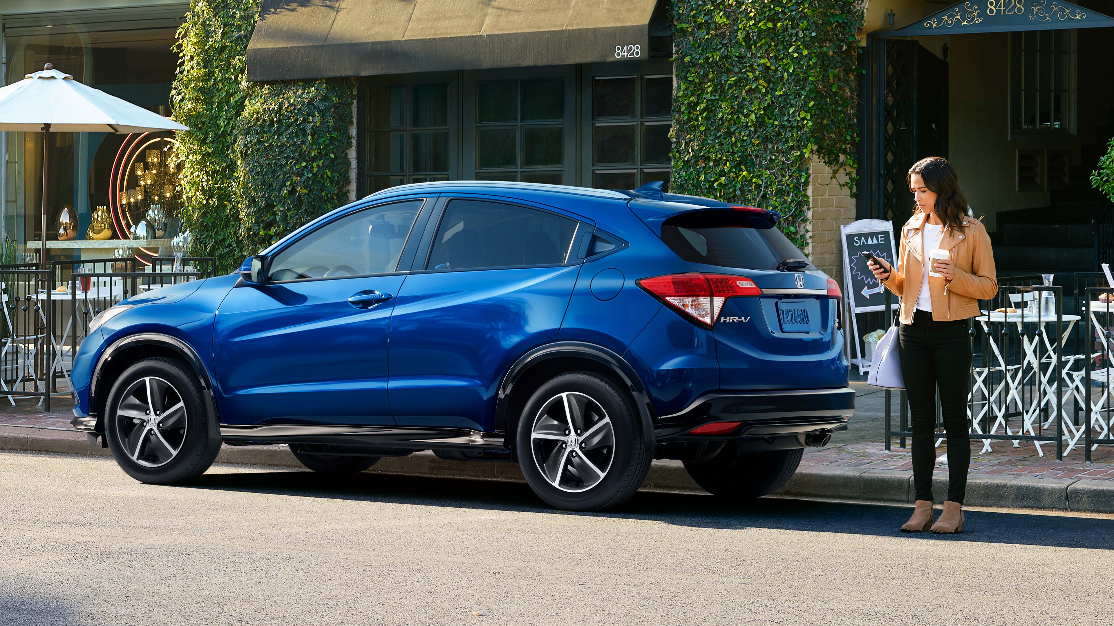 Rear driver-side view of the 2022 Honda HR-V Sport in blue parked in front of a café. 