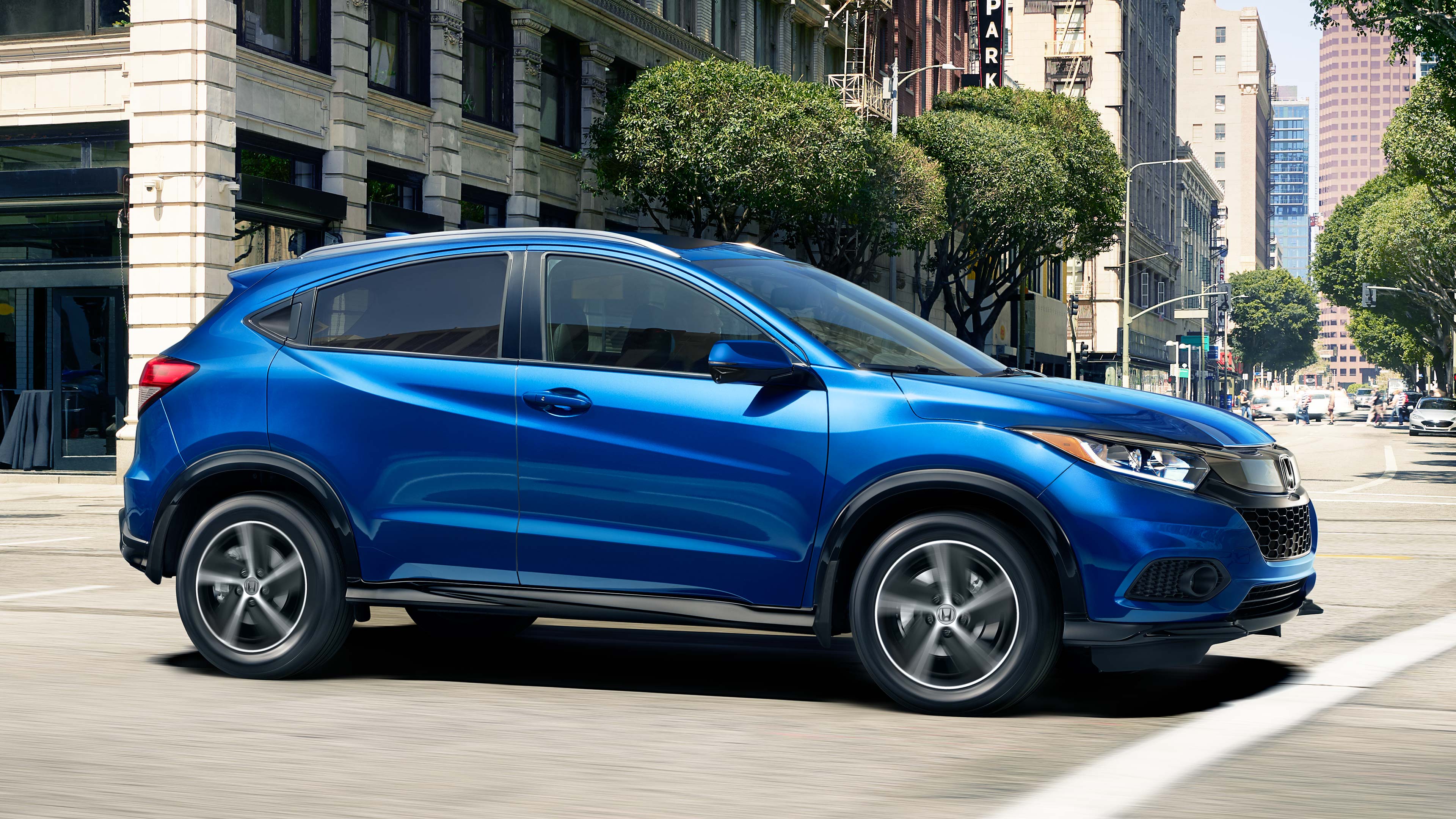 Front passenger-side view of the 2022 Honda HR-V Sport in blue driving down a city street. 