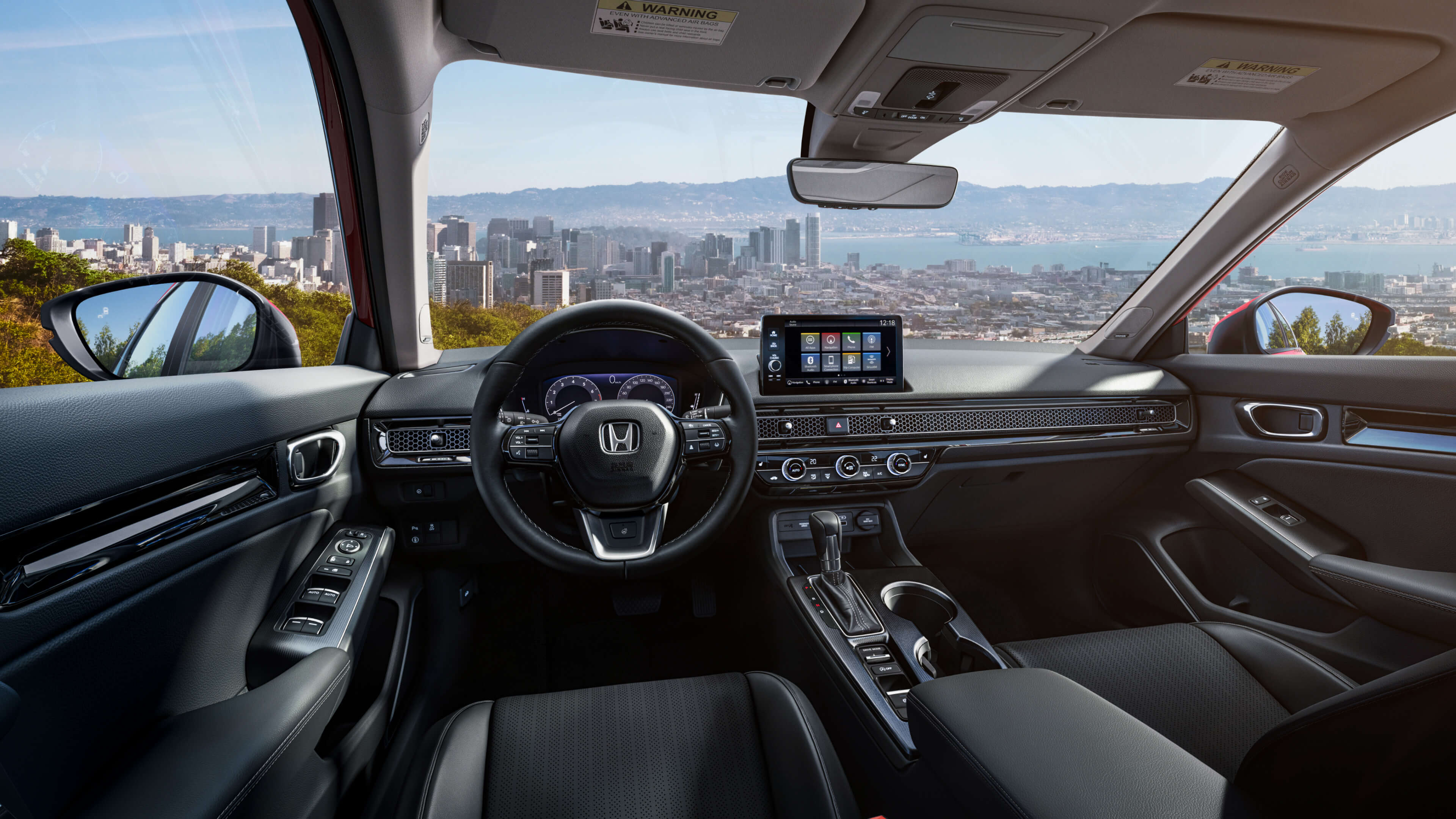Interior cockpit of a 2022 Honda Civic from the driver’s point of view. The shot overlooks a city on a bay as seen through the windshield from atop a peak.
