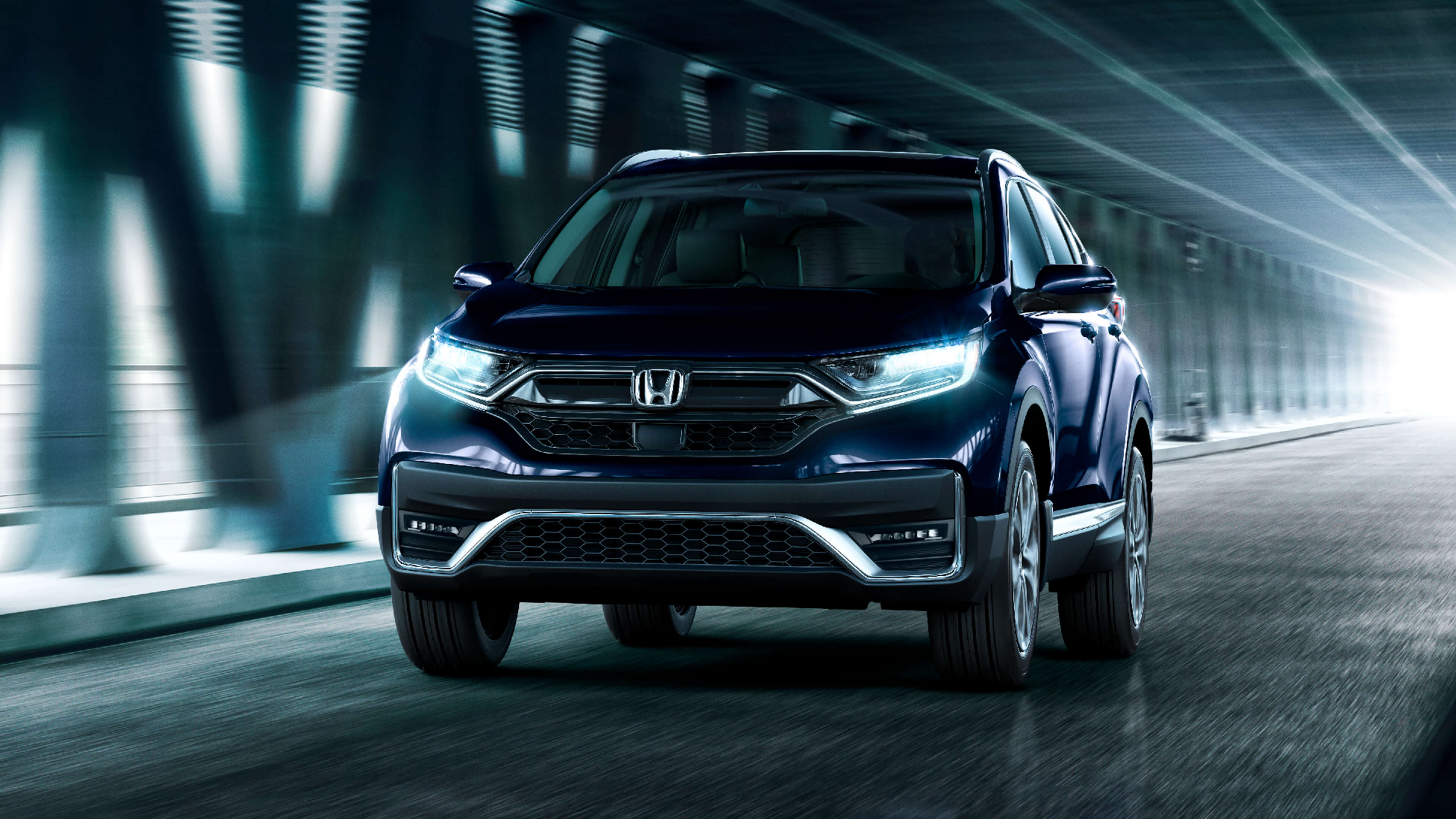 Front view of the 2021 Honda CR-V Touring in Obsidian Blue Pearl, driving under an urban overpass.