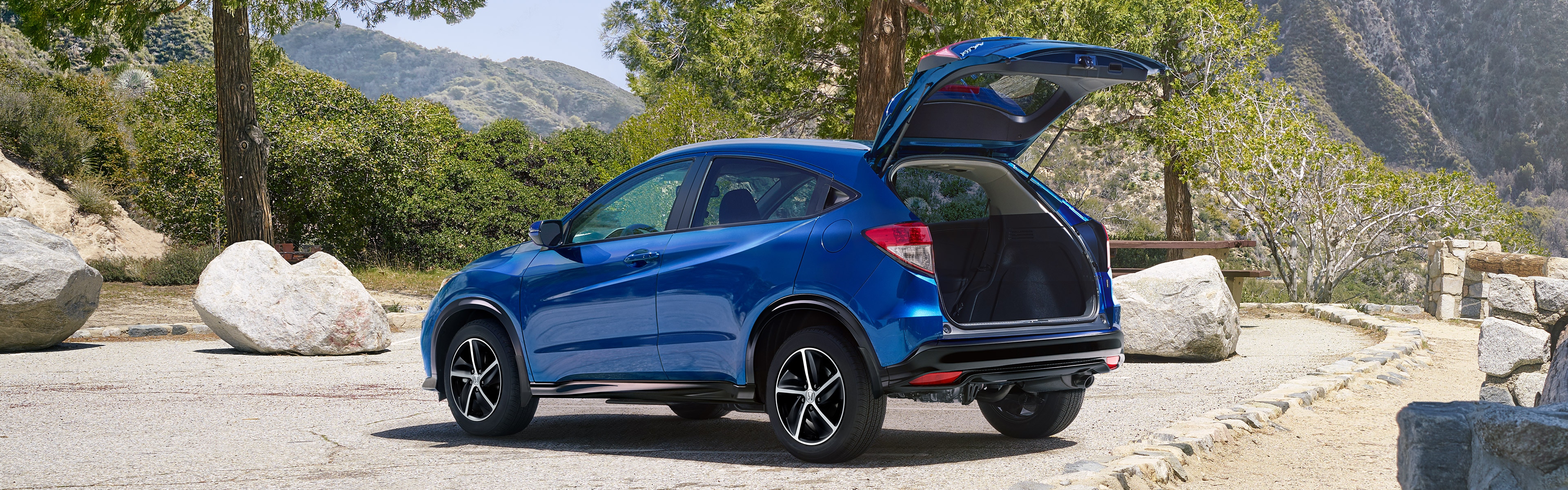Rear driver-side view of the 2022 Honda HR-V Sport in blue with rear tailgate open, parked in mountain location. 