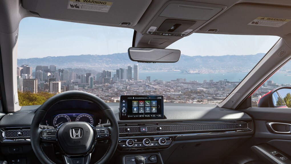 Image recadrée du pare-brise d’une Honda Civic 2022 du point de vue du conducteur. La scène par le pare-brise surplombe une ville située dans une baie.