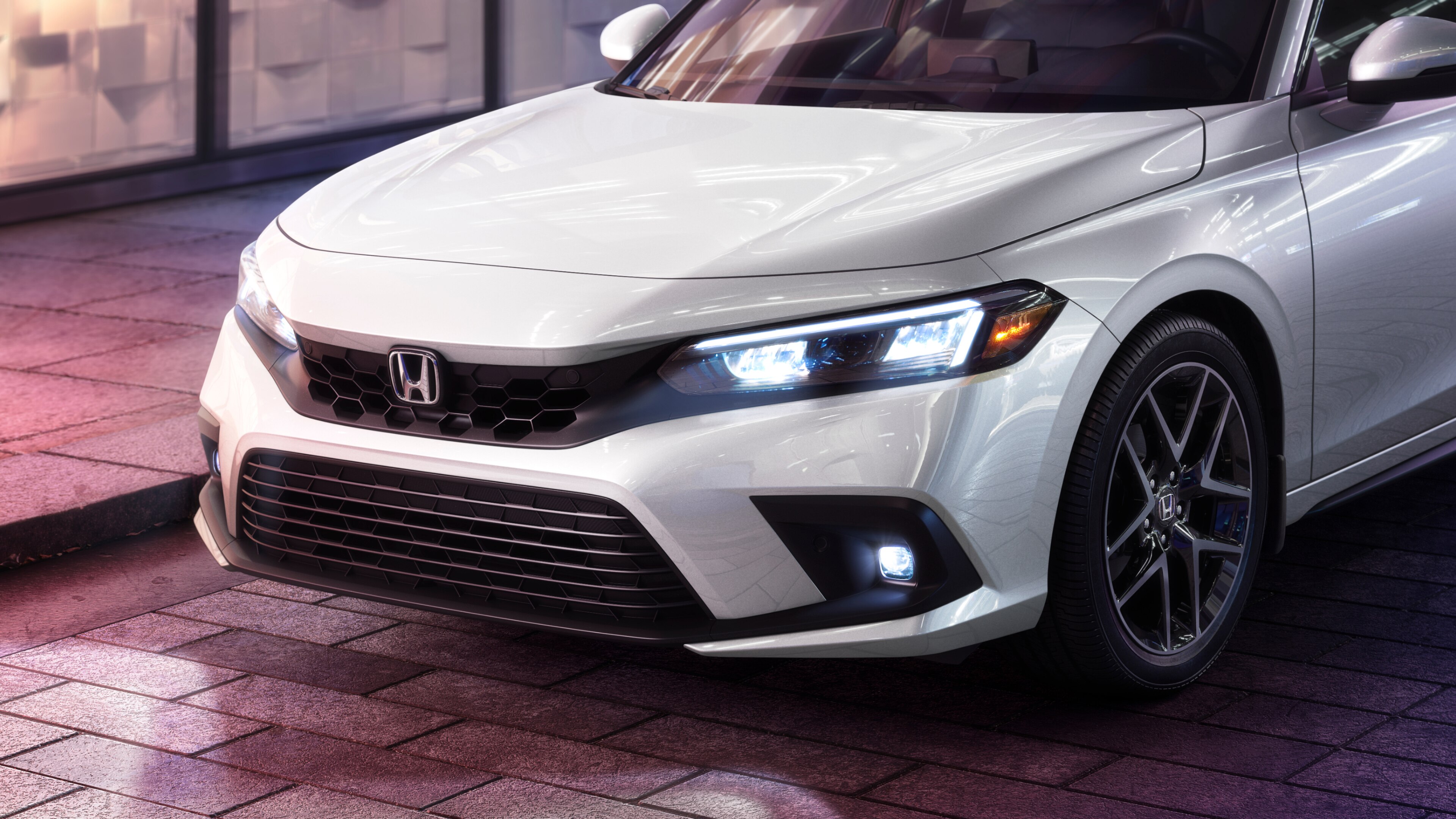 Side-angled close-up of white Honda Civic Hatchback with headlights shining on a brick road